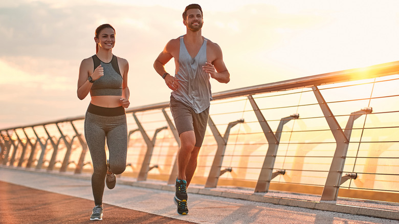 couple running together on boardwalk at sunset