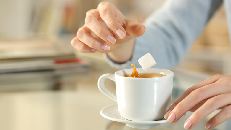 A woman puts a sugar cube in a cup of coffee