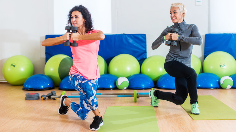 Two women perform curtsy lunges