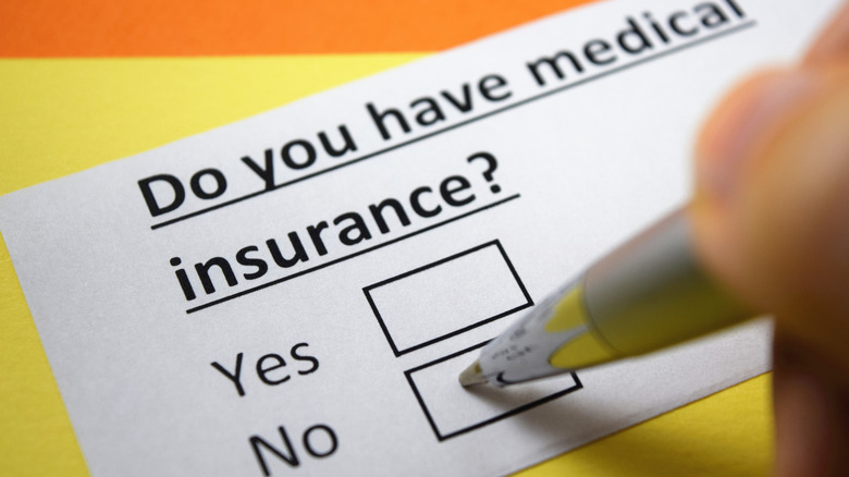 Hand checking a "No" box on a questionnaire asking if they have health insurance
