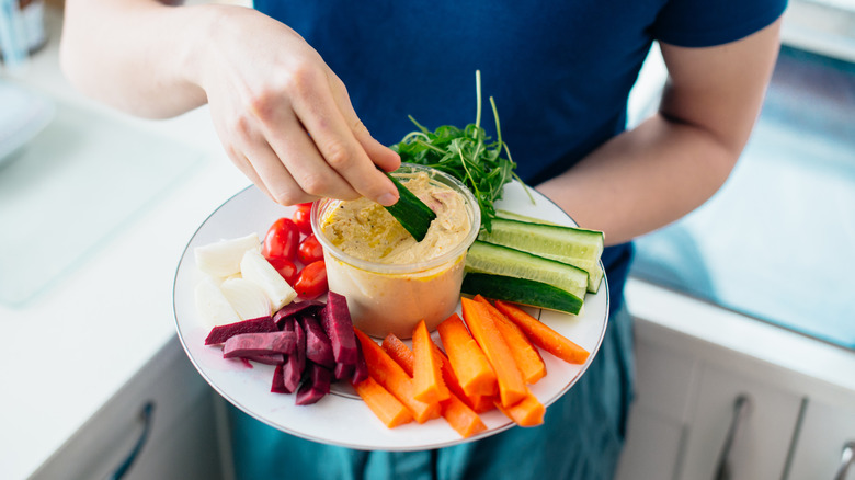 Hand dipping cucumber stick into hummus