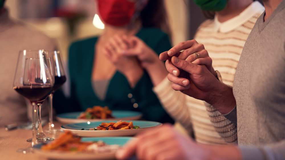people hold hands and pray around a meal