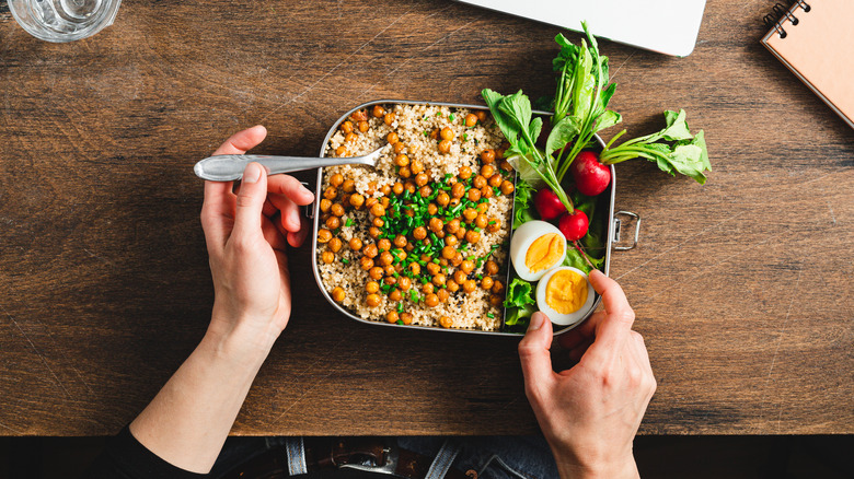 Hands eating bowl of chickpeas and quinoa