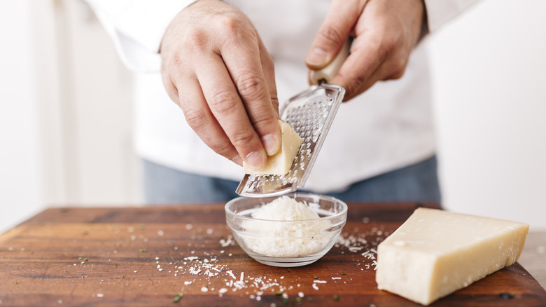 man grating fresh parmesan cheese into glass bowl