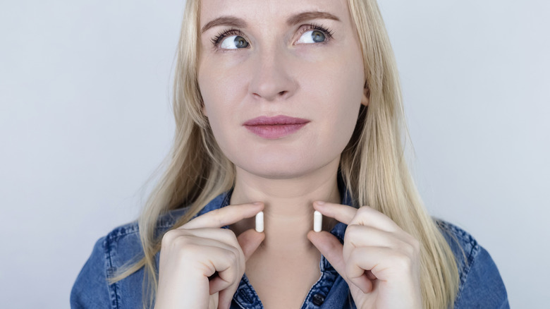 woman holding up thyroid pills to her throat