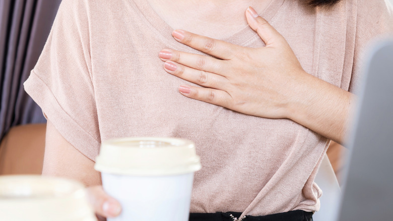 young woman holding heart while holding coffee