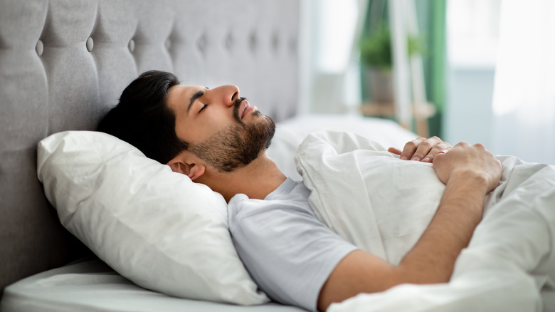 A man sleeping in a bed on his back