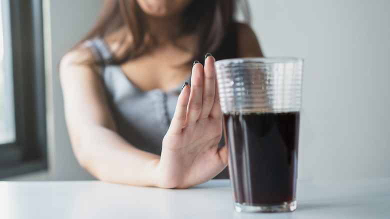 Person pushing away a full glass of soda