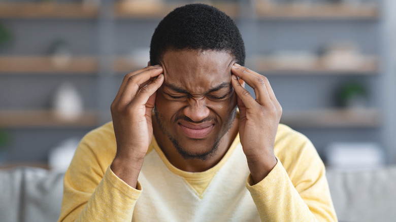 A man grimaces as he rubs his temples