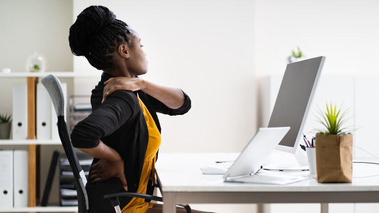 A woman at a desk rubs her neck and lower back