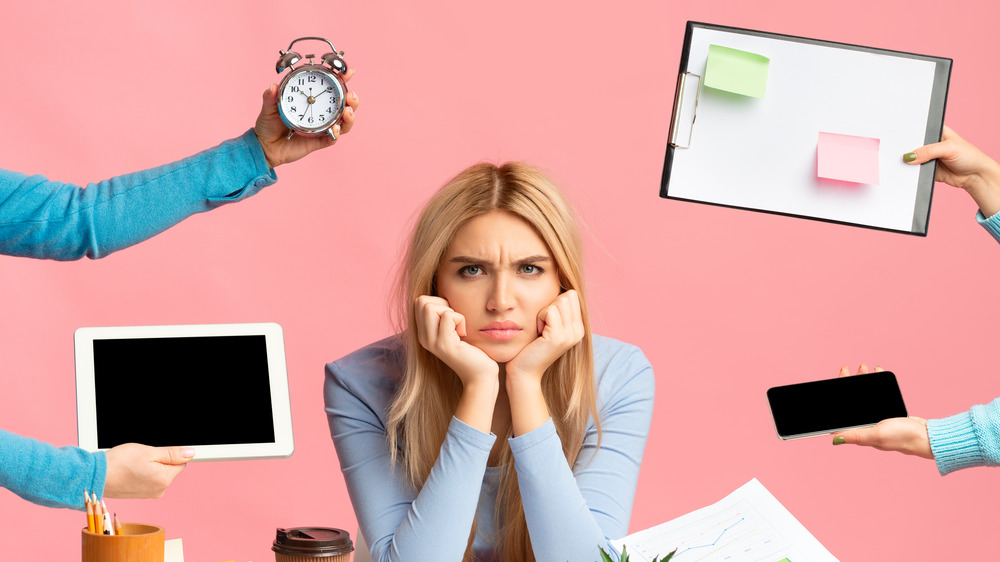 Woman sitting at a desk surrounded by hands foisting projects and calendars at her