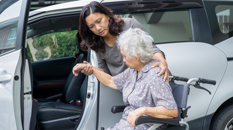 Woman assisting woman in wheelchair into car