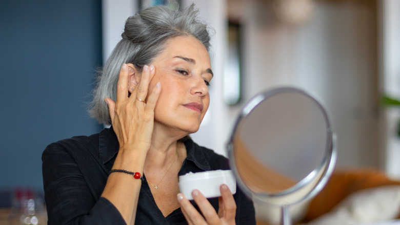 senior woman applying moisturizer to face in home setting
