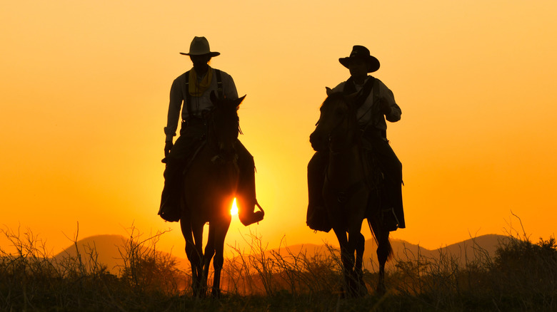 cowboys riding at sunset