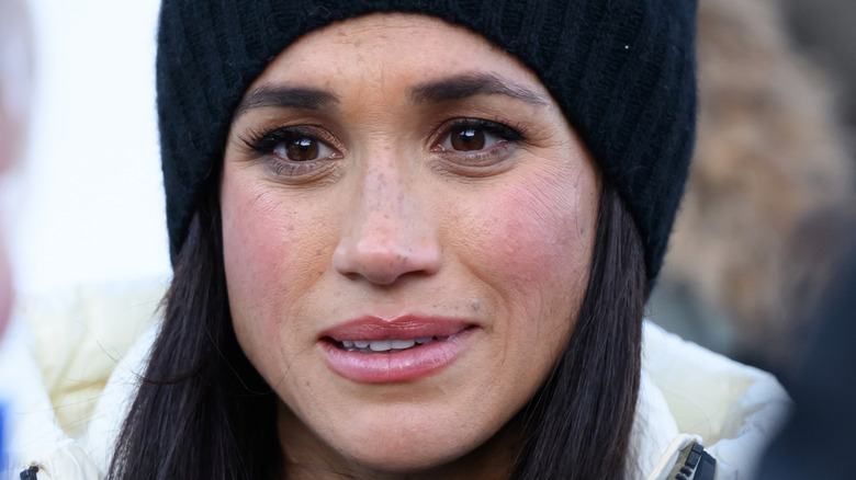 Close up on Meghan Markle in a black hat and a white puffy coat.