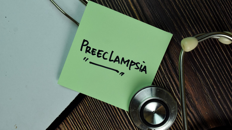 A wooden surface with a clipboard, a sticky note reading "Preeclampsia", and a stethescope.