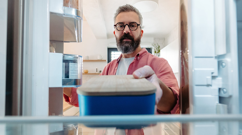 man taking container of leftovers out of the fridge