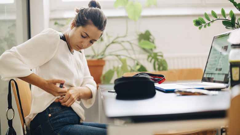 A woman in kitchen giving herself an insulin injection