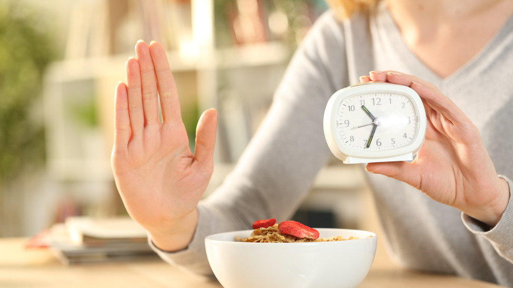 Woman holding clock denying food