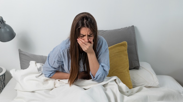 Woman sitting in bed, feeling nauseous 