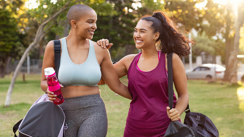 smiling friends walking holding gym bags