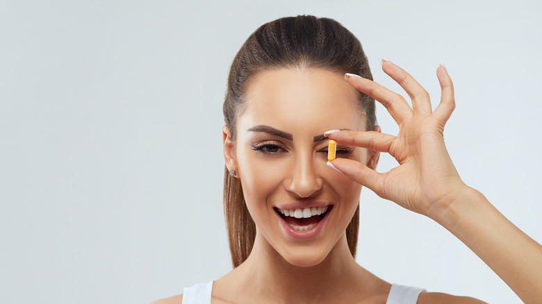 smiling woman holding vitamin over eye 