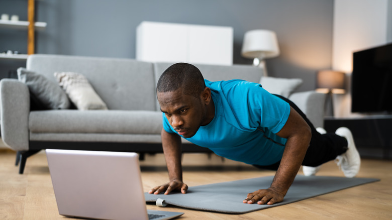 young man doing pushups in front of his laptop 