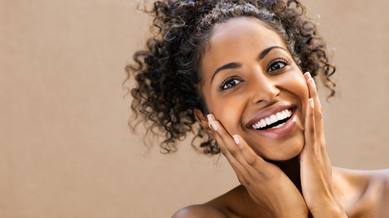 Curly-haired woman smiling and touching face