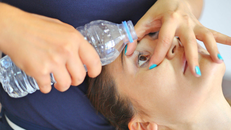 Person pouring bottled water over another person's eyes