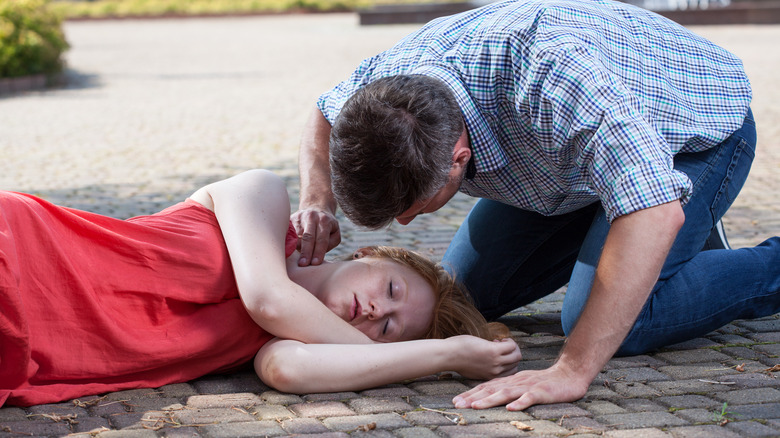 man checking pulse of unresponsive woman