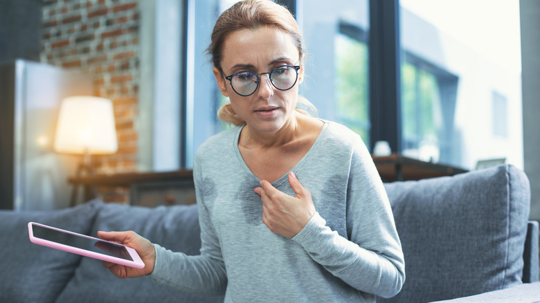 Woman sitting on couch holding a tablet sweating through shirt