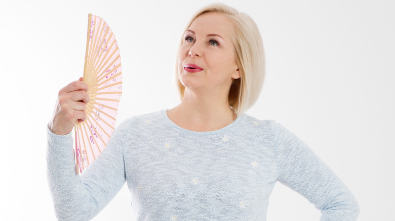 Woman in gray sweater holding a hand fan to cool off