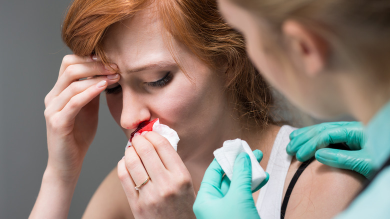 A woman with a nosebleed is helped by a nurse