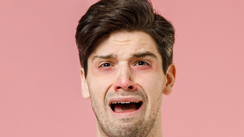 Man has red watery eyes stuffy nose holding tissues isolated on pastel pink color background.