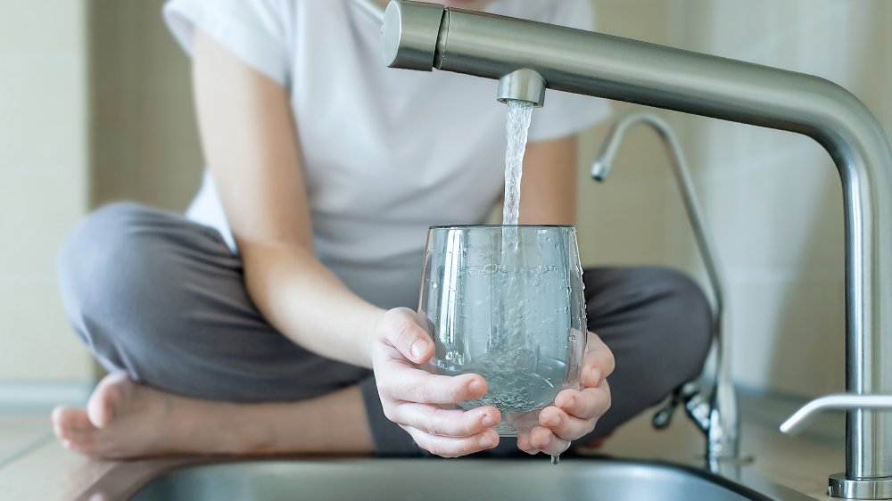 A child filling up a glass of water from the kitchen sink 