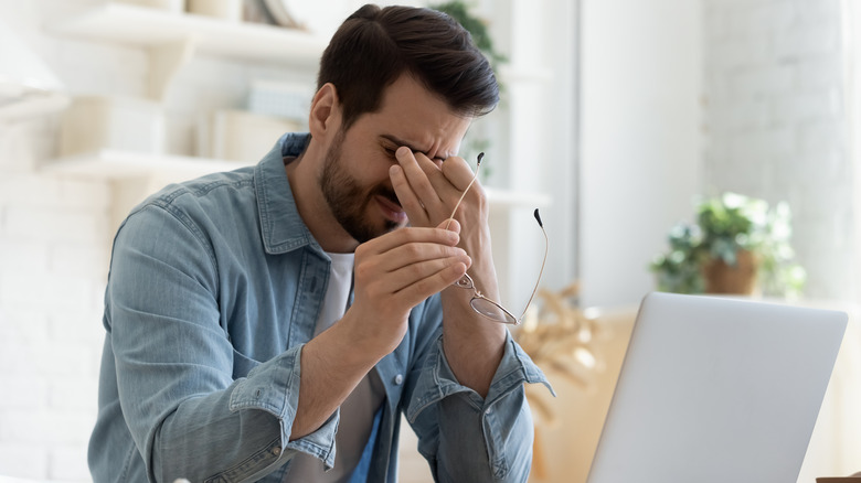 Sitting m﻿an holding glasses and rubbing eyes 