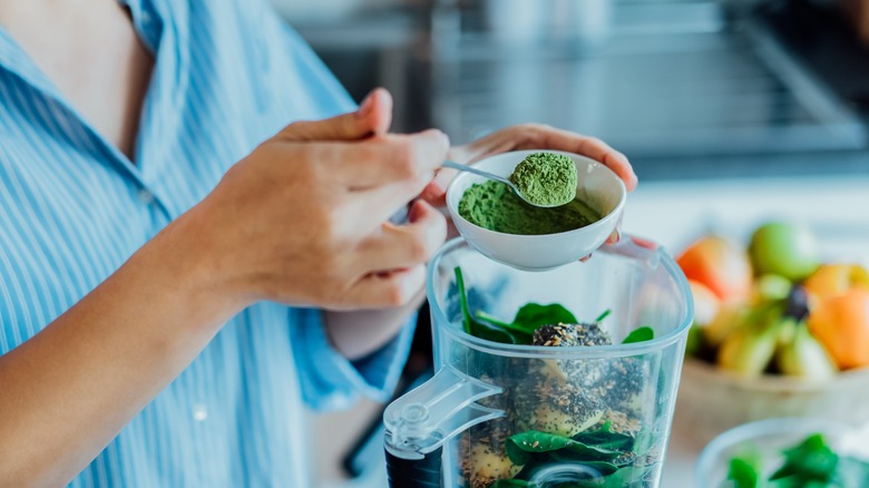 A woman adding ingredients to her blender