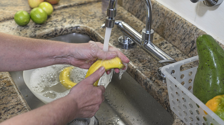 woman washing banana under faucet in kitchen