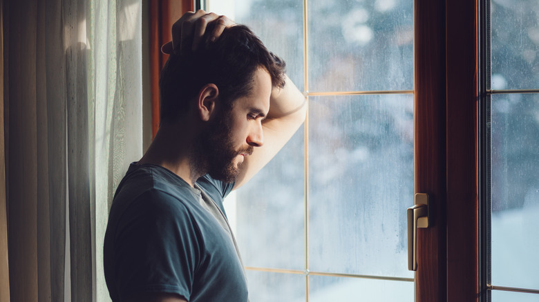 man standing at window looking sad