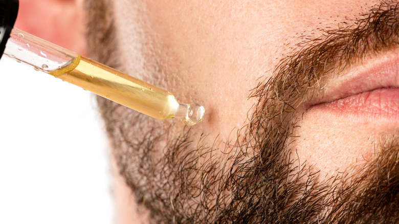 white man applying argan oil with dropper on skin