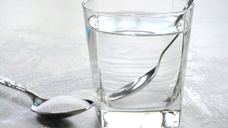 glass of water with spoon and teaspoon of salt