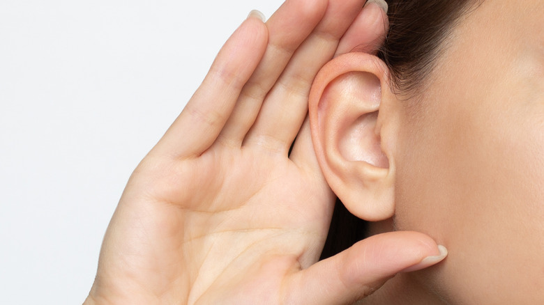 Close-up of a woman's hand touching her ear, signifying that she is listening.