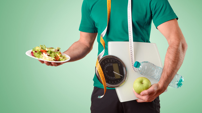 man juggling salad, scale and water bottle