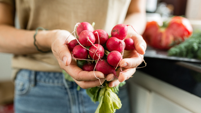 woman holding bunch of radishes in her hand at home