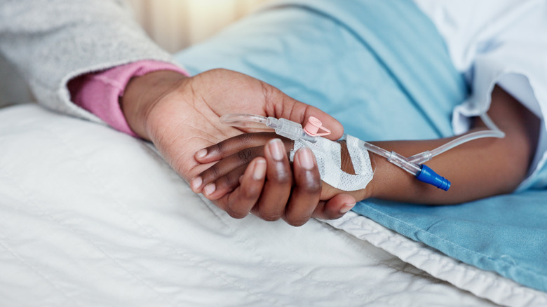 adult holding hand of child in hospital bed