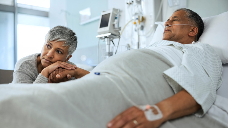 woman holding hand of man lying in hospital bed