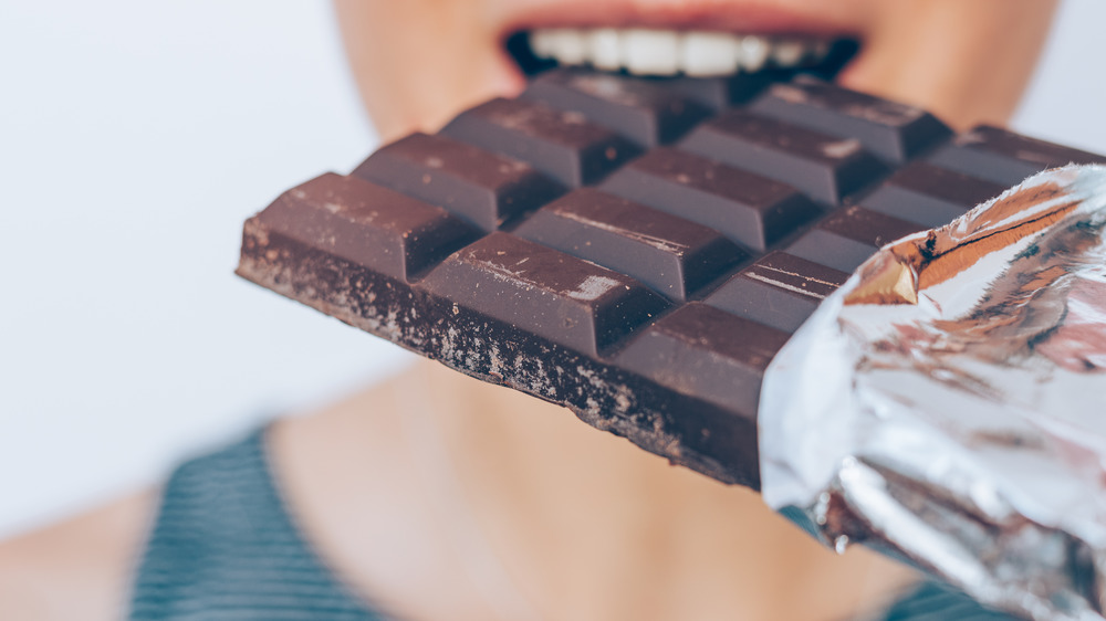 Closeup of mouth biting into a bar of chocolate