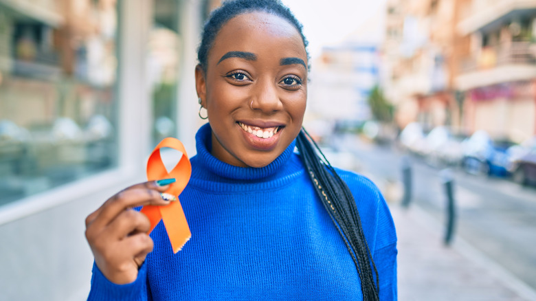 Woman in blue turtleneck sweater holding up orange awareness ribbon for Multiple Sclerosis
