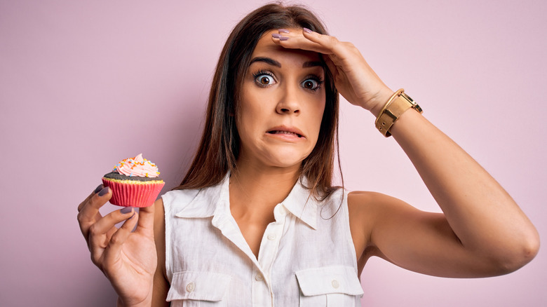 woman holding cupcake looking stressed