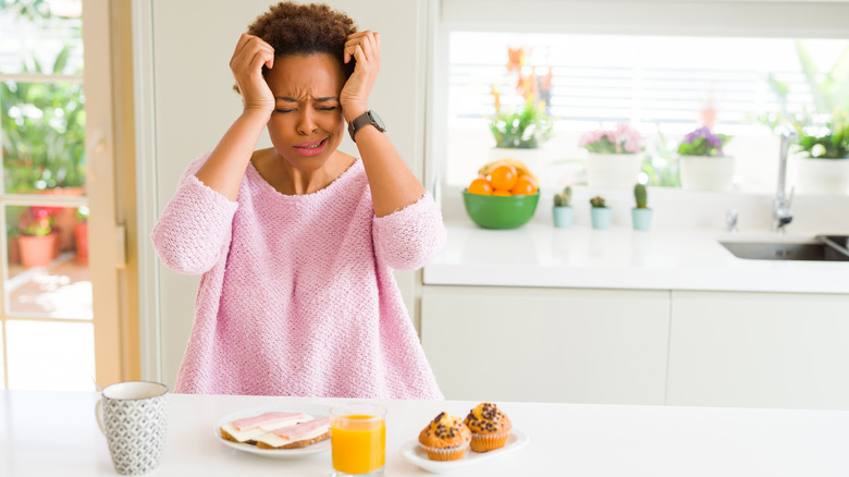 Grimacing woman holding head in kitchen